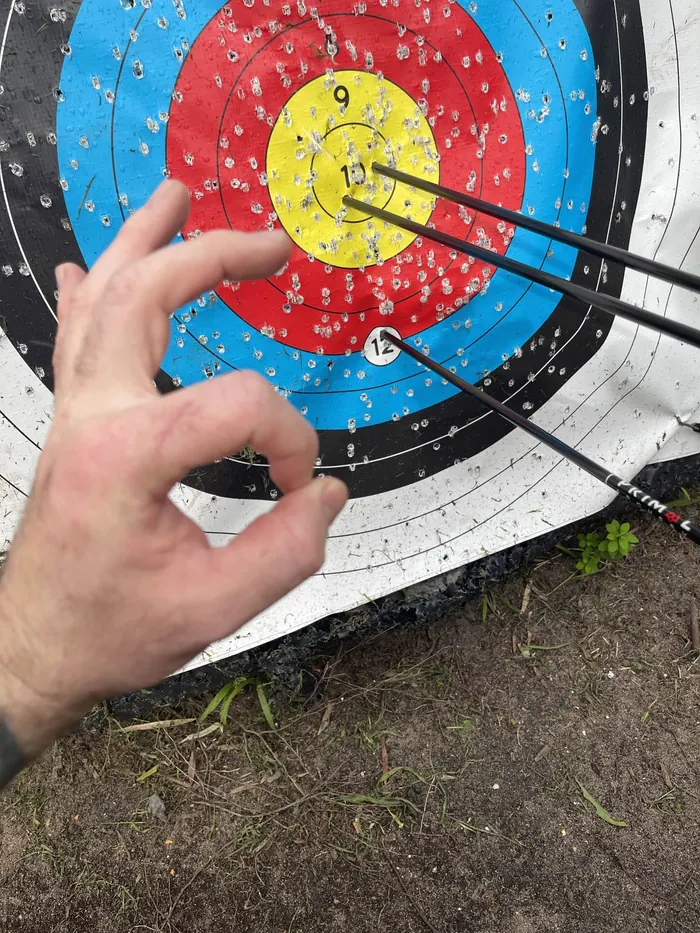 A hand makes an OK sign beside three arrows grouped in the gold of a well-used target