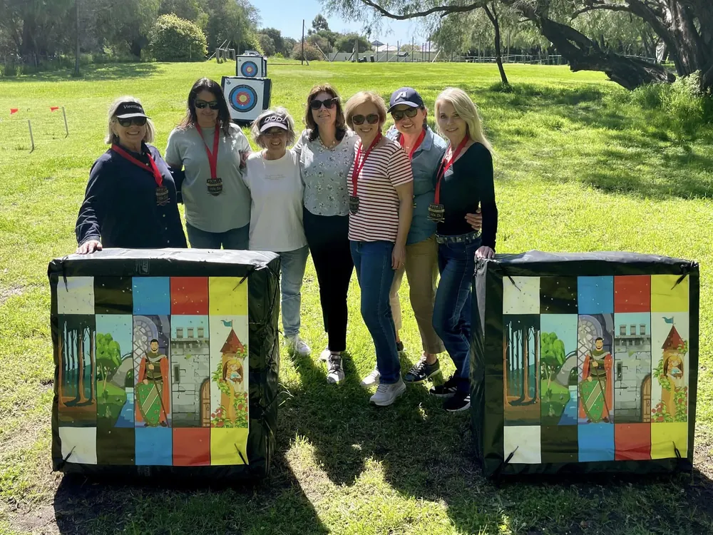 A group of friends with medals stand behind two painted game boxes on the grass