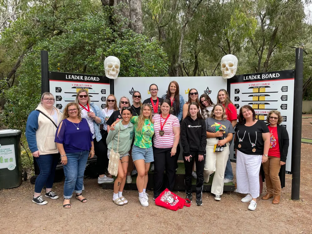 A group of archers pose in front of the Primal leaderboard wall, between two skull trophies