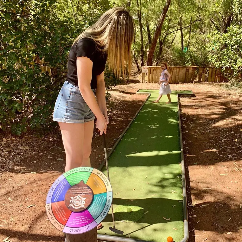 A player lines up a putt on the green mini golf course, a colourful challenge spinner beside the hole